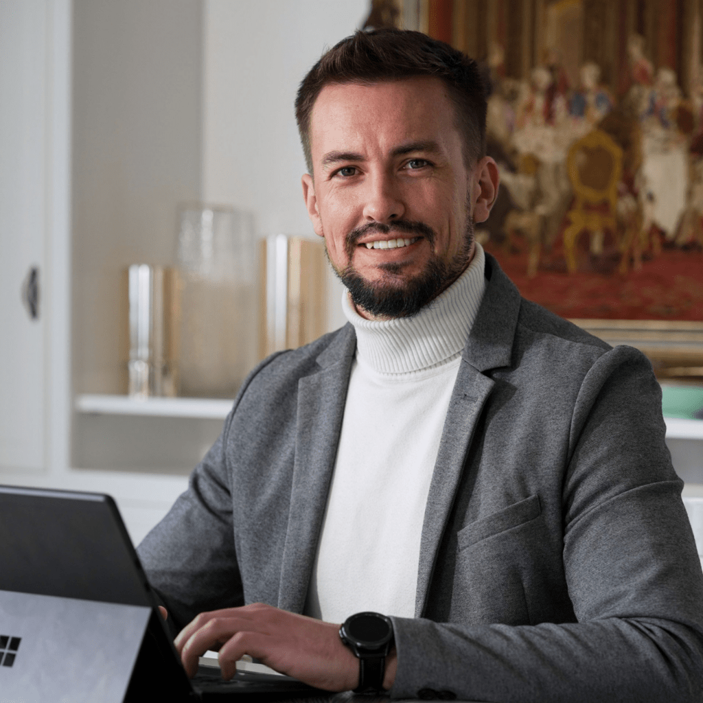 Porträt von Johann Steinwand, Inhaber von Verkaufsstarkes Webdesign, sitzend am Laptop, Gemälde im Hintergrund, lächeln und einladend