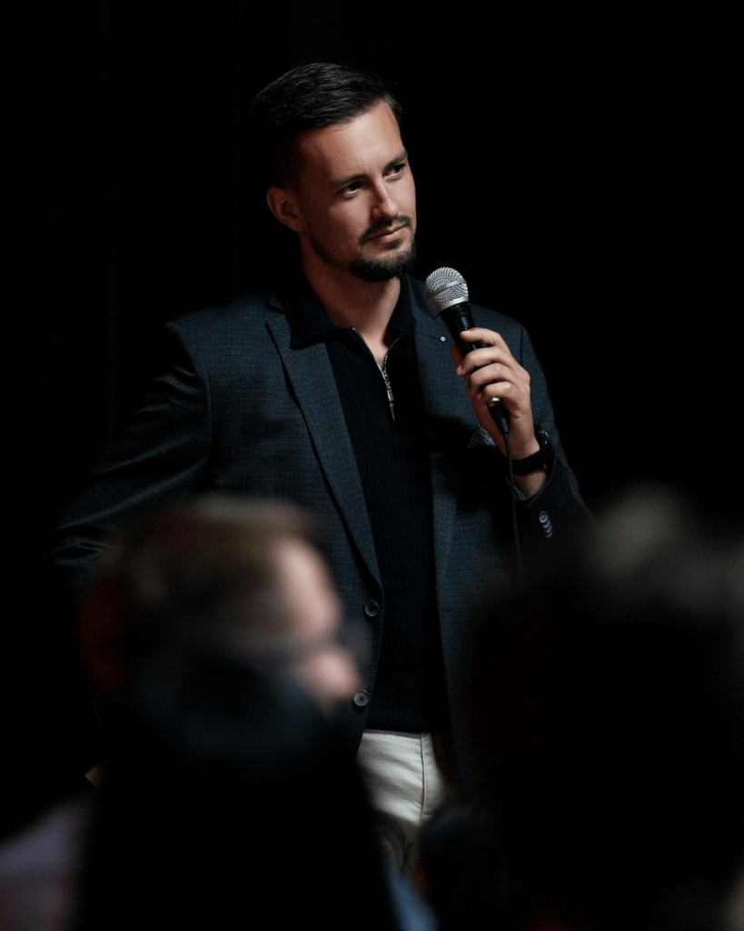 Johann Steinwand mit Mikrofon in der Hand, trägt Anzug, hält rede über selbstvermarktung auf einem marketingworkshop für selbstständige