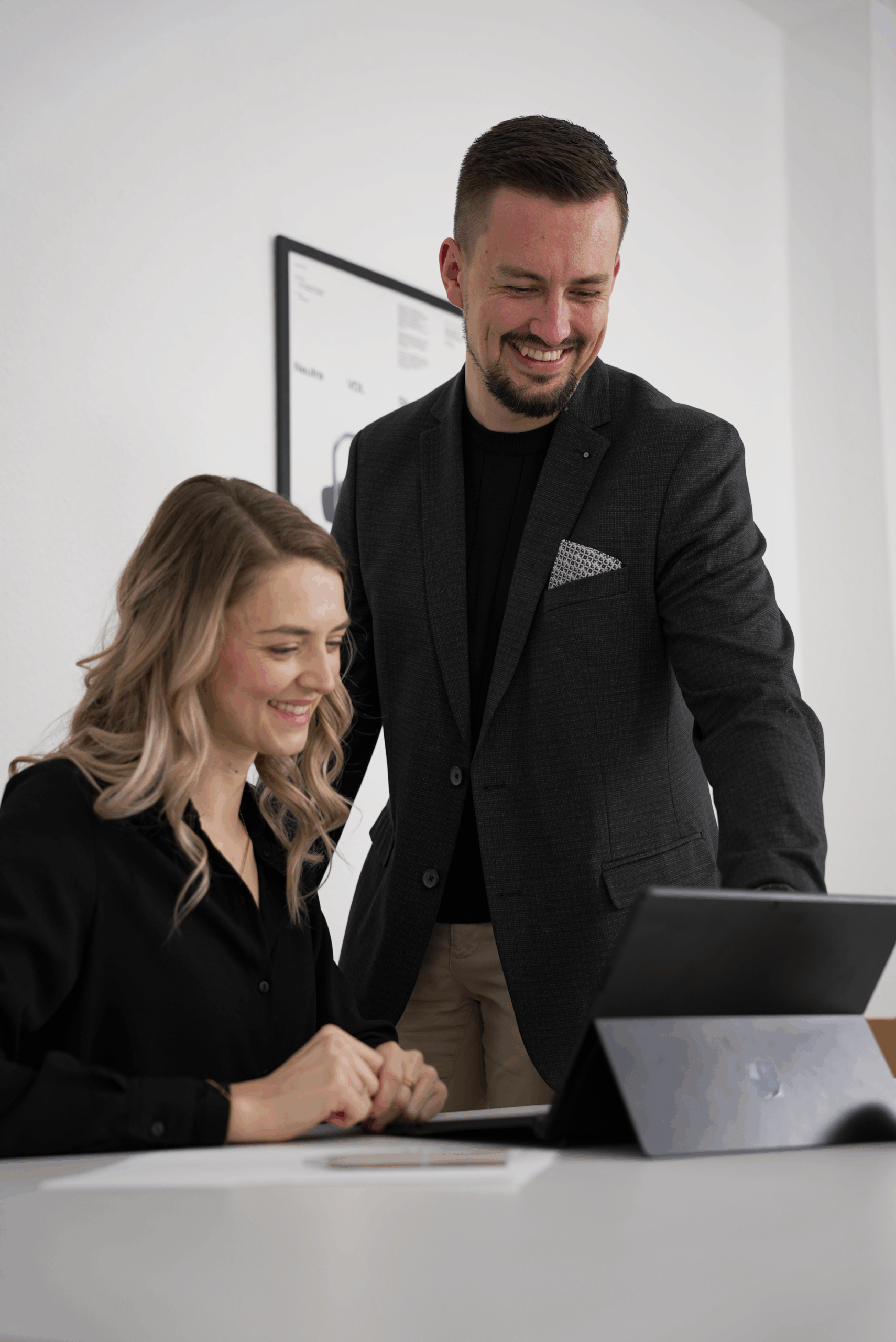 Johann Steinwand von Verkaufsstarkes Webdesign mit Kundin im Büro, beide lächeln, während sie am Laptop Ergebnisse von Website und SEO anschauen.